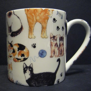 May include: White ceramic mug with a colourful cat pattern. The mug features a variety of cats in different poses, including a calico cat, a black cat, and a tabby cat. The mug also features a blue ball of yarn and paw prints.