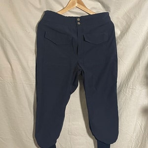 May include: Dark blue pants with a button fly and two large pockets on the front. The pants have a cuffed hem.
