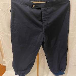 May include: A pair of dark blue pants with a button fly and elastic cuffs. The pants are made of a thick, durable fabric and have a relaxed fit.