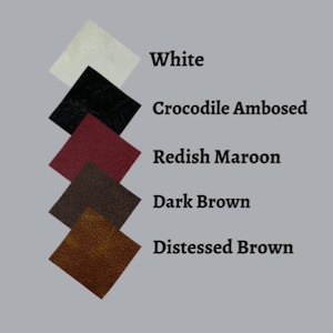May include: A selection of leather swatches in shades of white, black crocodile embossed, reddish maroon, dark brown, and distressed brown. Each swatch is labelled with its colour name against a grey background.