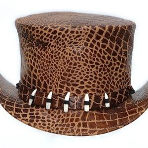 May include: A brown leather top hat with a reptile-like texture. The hat features a wide brim and a decorative band with white and black accents. The hat is a unique accessory.