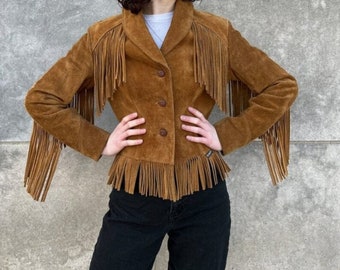 May include: A brown suede jacket with fringe detailing on the sleeves and hem. The jacket has a button-up front and a classic collar. The fringe adds a Western-inspired flair to the outerwear.