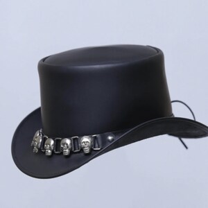 May include: A black leather top hat with a wide brim. The hat features a silver-colored band adorned with skull-shaped embellishments. The hat is a classic style, suitable for various occasions.
