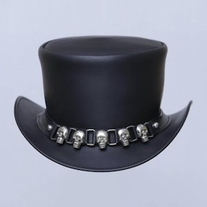 May include: Black leather top hat with a wide brim. The hat features a decorative band around the crown adorned with silver-colored skull accents. A stylish accessory for themed events or everyday wear.