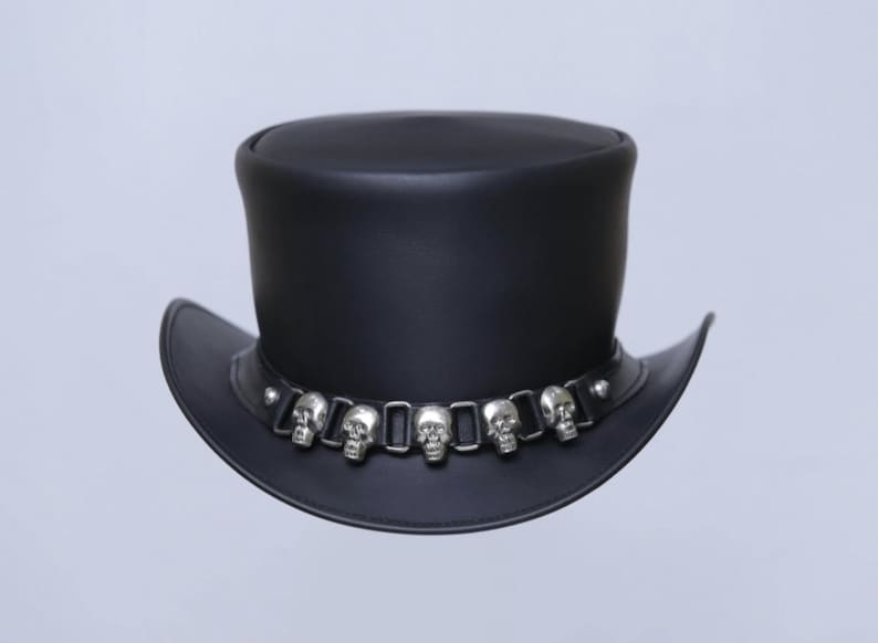May include: Black leather top hat with a wide brim. The hat features a decorative band around the crown adorned with silver-colored skull accents. A stylish accessory for themed events or everyday wear.