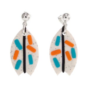 Puede incluir: Un par de pendientes colgantes con un diseño blanco moteado en forma de hoja. Los pendientes presentan acentos rectangulares naranjas y turquesas, una raya vertical negra y postes plateados.