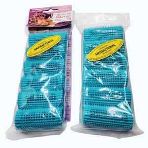 Puede incluir: Dos paquetes de rulos turquesa. Cada paquete contiene varios rulos, visibles a través del embalaje de plástico transparente. Los paquetes tienen etiquetas amarillas que dicen "Protección Antibacteriana". Un paquete tiene una etiqueta rosa y morada con texto.