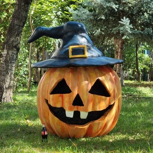 Könnte beinhalten: Ein großer orangefarbener Kürbis mit einem schwarzen Hexenhut und einem geschnitzten Jack-o'-Lantern-Gesicht. Der Kürbis steht auf einem grünen Rasen.