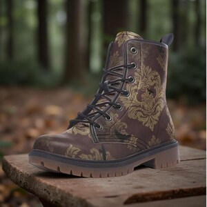 May include: A brown ankle boot featuring a repeating gold damask pattern, black laces, silver-toned metal eyelets, and a thick, textured brown rubber sole. The boot has a pull tab at the heel and a rounded toe, showcasing a structured design.