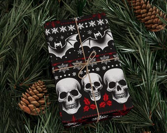 Puede incluir: Papel de regalo negro con un patrón repetido de calaveras blancas, murciélagos, copos de nieve y hojas de acebo rojas. El papel está atado con hilo y colocado sobre un fondo de agujas de pino y piñas.