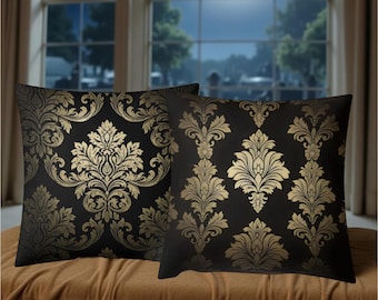 May include: Two black throw pillows with a gold damask pattern. The pillows are square and rest on a brown surface. The background shows a window with a full moon and trees.