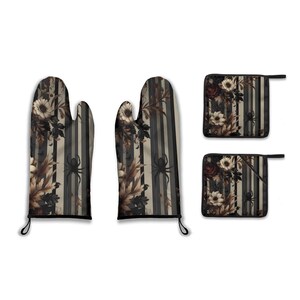May include: A kitchen set featuring oven mitts and pot holders with a floral and spider design. The pattern includes cream flowers, brown leaves, and black spiders on a striped grey and black background. The oven mitts have black hanging loops.