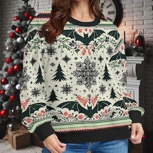 May include: A cream-coloured sweatshirt with a festive Christmas design. The design includes bats, snowflakes, Christmas trees, and floral elements in red, green, and black. The sweatshirt has black cuffs and a black collar.