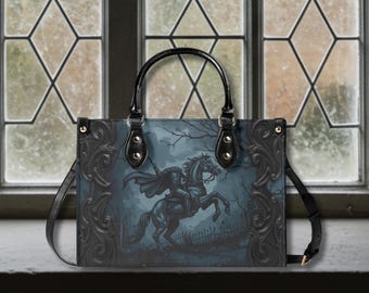 May include: Black tote bag featuring a spooky illustration of a headless horseman on a rearing horse in a graveyard scene. The bag has a black handle and shoulder strap, with decorative black trim and gold-colored rivets.