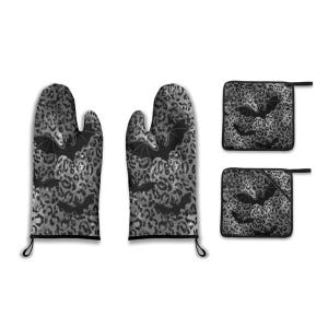 Op de afbeelding: Een set keukentextiel met een zwart-grijze luipaardprint en vleermuissilhouetten. De set bevat twee ovenwanten en twee pannenlappen. De ovenwanten en pannenlappen hebben zwarte biezen en ophanglussen.