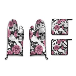 Könnte beinhalten: Ein Küchentextil-Set mit Totenkopf-, Rosen- und Schmetterlingsmuster auf weißem Hintergrund. Das Set enthält zwei Ofenhandschuhe und zwei Topflappen. Die Ofenhandschuhe und Topflappen haben eine schwarze Einfassung und Aufhängeschlaufen.