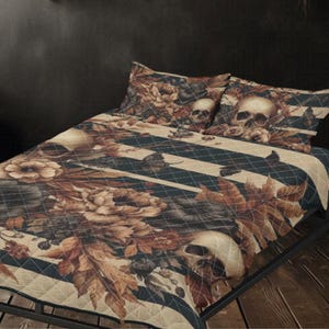 Pode incluir: Um conjunto de edredão bege e preto com um padrão floral e de caveira. O edredão apresenta grandes flores, folhas e caveiras, com riscas pretas e brancas. O conjunto inclui duas fronhas. A roupa de cama está numa estrutura de cama de metal preto.