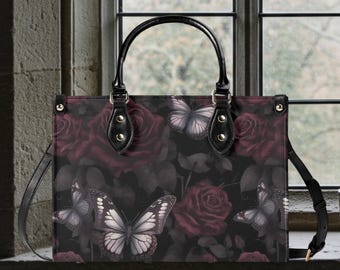 Può includere: Borsa tote nera con un motivo floreale e a farfalle. La borsa ha un manico nero e una tracolla staccabile. Il motivo include rose rosso scuro e farfalle bianche su sfondo nero. La borsa è di forma rettangolare.