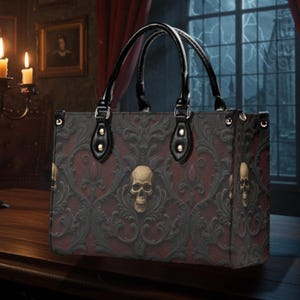 Może przedstawiać: Prostokątna torba typu tote o gotyckim designie. Torba ma ciemnoczerwony i czarny wzór damasceński z akcentami czaszek i kwiatów. Ma czarne uchwyty i wykończenia ze złotym osprzętem.
