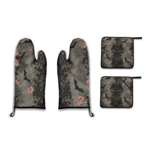 Könnte beinhalten: Ein Küchenset mit Ofenhandschuhen und Topflappen im gotischen Stil. Der graue Stoff ist mit schwarzen Damastmustern, rosa Rosen und Fledermaussilhouetten versehen. Die Ofenhandschuhe haben eine schwarze Einfassung und Aufhängeschlaufen.