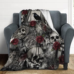 Könnte beinhalten: Eine gotische Decke mit einem sich wiederholenden Muster aus Totenköpfen, Rosen und verzierten Rahmen in Grau- und Schwarztönen. Ein schwarzer Rabe sitzt auf dem Design. Die Decke ist über einem grauen Sessel drapiert.