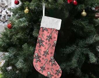 Puede incluir: Un calcetín navideño con fondo rosa, con un estampado de hombrecitos de jengibre esqueleto, bastones de caramelo y copos de nieve. El calcetín tiene un puño de piel sintética blanca y un lazo blanco para colgar. Cuelga de un árbol de Navidad.