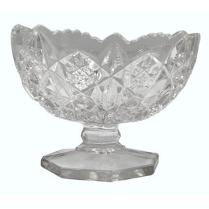Puede incluir: Cuenco de postre de cristal tallado transparente con borde festoneado. El cuenco presenta un diseño de diamantes y estrellas y se apoya sobre una base de pedestal. Ideal para servir postres.
