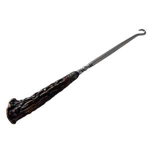May include: A vintage-style crochet hook with a dark brown, textured handle and a silver-colored metal shaft. The handle appears to be made of antler or a similar material. The hook is designed for crafting and textile work.