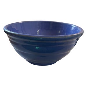Può includere: Una ciotola in ceramica blu profondo con una finitura lucida e una serie di creste orizzontali che circondano l'esterno. La ciotola presenta un bordo circolare ampio e aperto e una base liscia e arrotondata, con un colore solido uniforme.