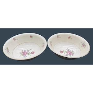 May include: Two off-white ceramic bowls featuring a central floral motif with pink roses and green leaves. The interior rims are decorated with smaller scattered floral sprigs and finished with a thin gold-colored trim along the edges.
