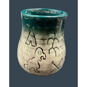 May include: A teal ceramic vase with a white glaze and black hand-painted designs. The vase has a rounded bottom and a wide opening.