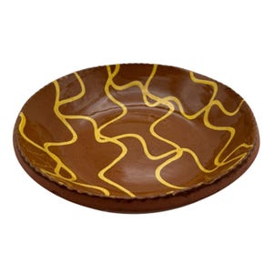 May include: A brown ceramic plate with a wavy gold pattern. The plate has a slightly raised rim and a smooth, glossy finish. The design is a series of interconnected, abstract lines.