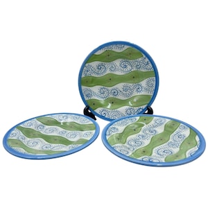 May include: Three ceramic plates with a blue rim and a green and white wave pattern. The plates are round and oval, with a blue rim. The wave pattern is green and white with blue swirls.