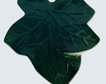 May include: A glossy, dark green ceramic leaf-shaped dish. The dish features detailed veining and a smooth, reflective surface. The design is a stylized representation of a leaf, perfect for serving or decoration.