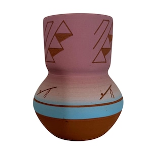 Può includere: Un vaso in ceramica fatto a mano con un design unico. Il vaso presenta una parte superiore viola chiaro con forme geometriche marroni, una striscia azzurra e una base marrone. Il vaso ha una forma bulbosa e viene probabilmente utilizzato per scopi decorativi.