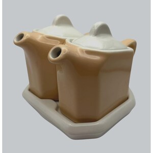 May include: A matching cream and sugar set, comprising two square ceramic containers with lids and a tray. The containers are tan with white lids and spouts. The tray is white. Ideal for serving tea or coffee, the set is a classic design.