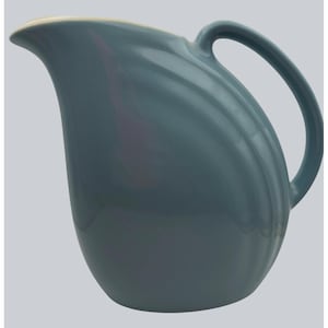 Puede incluir: Una jarra de cerámica color turquesa con un pico curvo y un asa grande y arqueada. La jarra tiene un acabado liso y brillante y un borde de color crema. El diseño es simple y elegante, adecuado para servir bebidas.