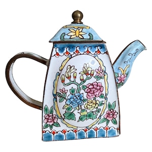 May include: A decorative, vintage teapot with a white enamel body and a floral design. The teapot features a blue lid and spout, a brass handle, and a brass finial. The floral design includes pink, blue, and yellow flowers.