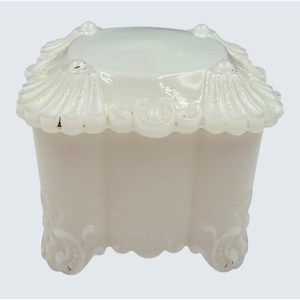 May include: A white, antique-style trinket box with a scalloped lid and ornate detailing. The box has a square shape with rounded corners and sits on four small feet. The box is made of a solid, opaque material.