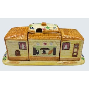 Puede incluir: Un juego de condimentos con temática de cocina de cerámica con techo amarillo y paredes beige. El juego incluye un salero, un pimentero y un recipiente central con tapa. Las palabras "OLDE FIRESID" están impresas en la parte delantera. El juego está sobre una base amarilla.