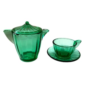 Può includere: Una teiera in vetro verde smeraldo traslucido con coperchio abbinato e una singola tazza da tè appoggiata su un piattino. Sia la teiera che la tazza presentano un motivo a coste verticali, creando un'estetica coerente in tutto il set.