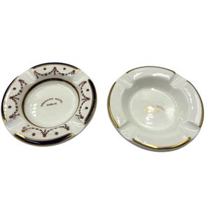 May include: Two white ceramic ashtrays. One has a blue and maroon decorative border and the text "Gresham Hotel Dublin". The other ashtray has a gold rim and the same text in gold.