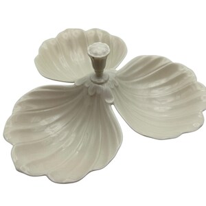 May include: A white, three-section serving dish shaped like a flower. It features three large, petal-shaped sections and a central stem with a bud-like detail. The surface has a subtle, ribbed texture.