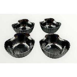 May include: Four small, dark gray decorative bowls with a woven basket design. The bowls have a scalloped edge and a shiny, reflective interior. The bowls are arranged in a square formation on a white background.
