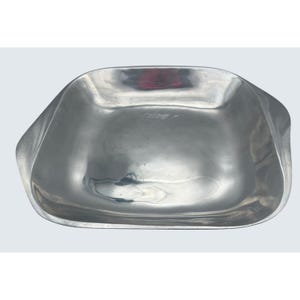 May include: A brushed silver metal serving bowl with a square shape and gently curved sides. The bowl has a smooth, reflective surface and a slightly textured appearance. The design is simple and modern, suitable for serving food or as a decorative piece.
