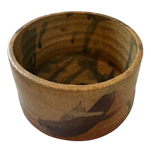 Może przedstawiać: Biały ceramiczny kubek z czarnym uchwytem i napisem "But First, Coffee" pogrubioną, czarną czcionką. Kubek jest ustawiony na neutralnym tle, podkreślając jego prosty design.