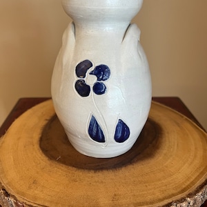 May include: A white ceramic vase with blue floral designs. The vase has two handles and a rounded body.