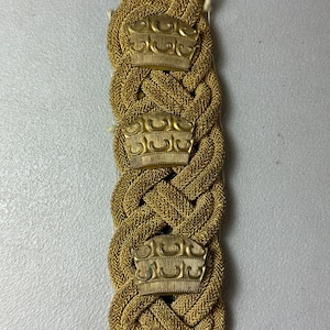 May include: Gold braided cord with three decorative metal accents. Each accent features a stylised crown design.