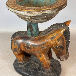 Puede incluir: Una escultura de madera de un caballo con un cuenco en la espalda. El cuenco está pintado de azul y blanco, y el caballo está pintado de marrón y negro.
