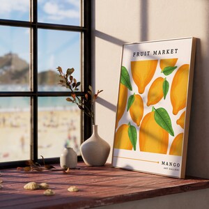 May include: A framed print with a white background and a pattern of yellow lemons and green leaves. The text "FRUIT MARKET" is at the top of the print and "MANGO ART GALLERY" is at the bottom.